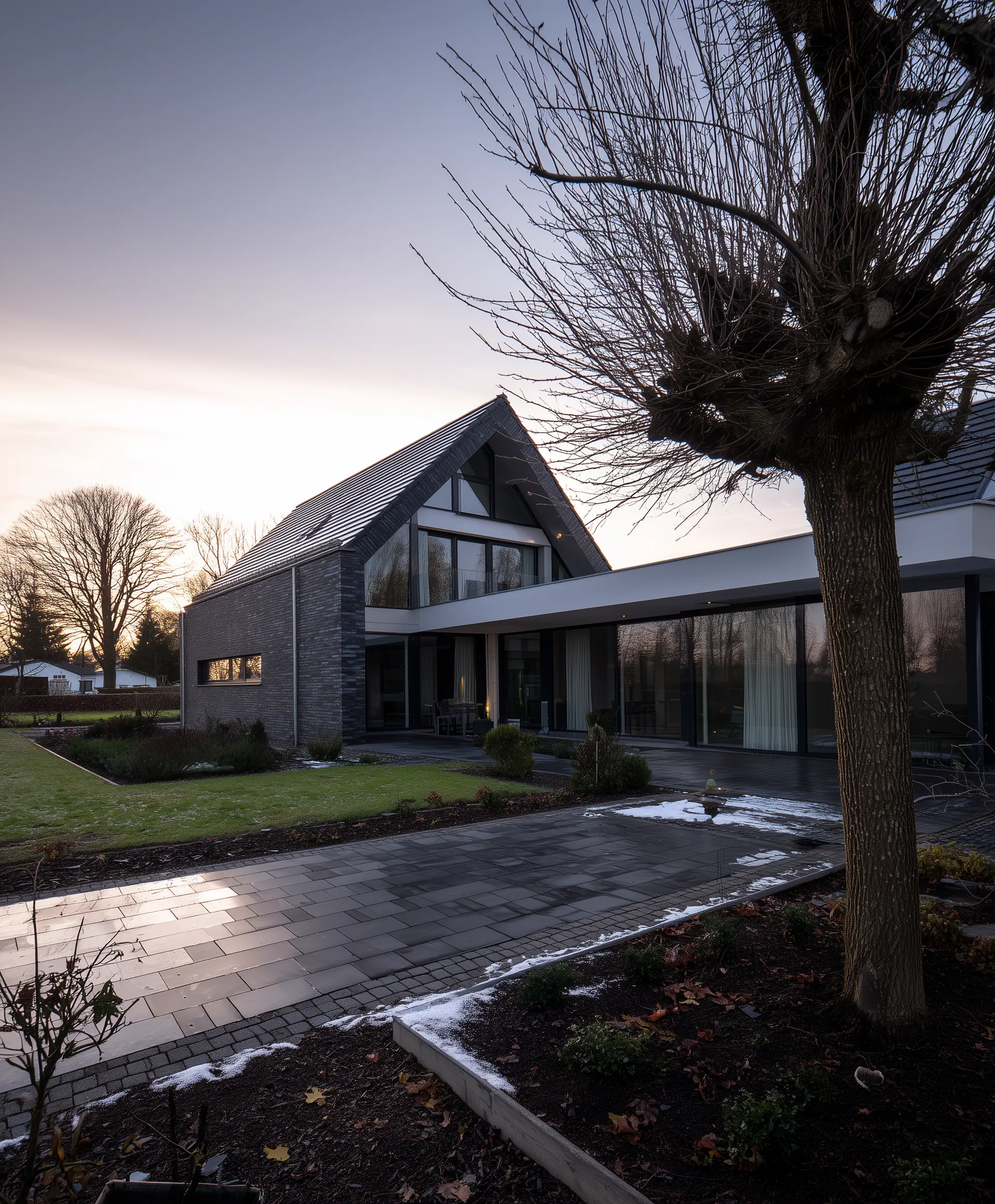 Modernes Einfamilienhaus mit großen Glasfronten und dunkler Ziegelverkleidung, umgeben von einem gepflegten Garten.