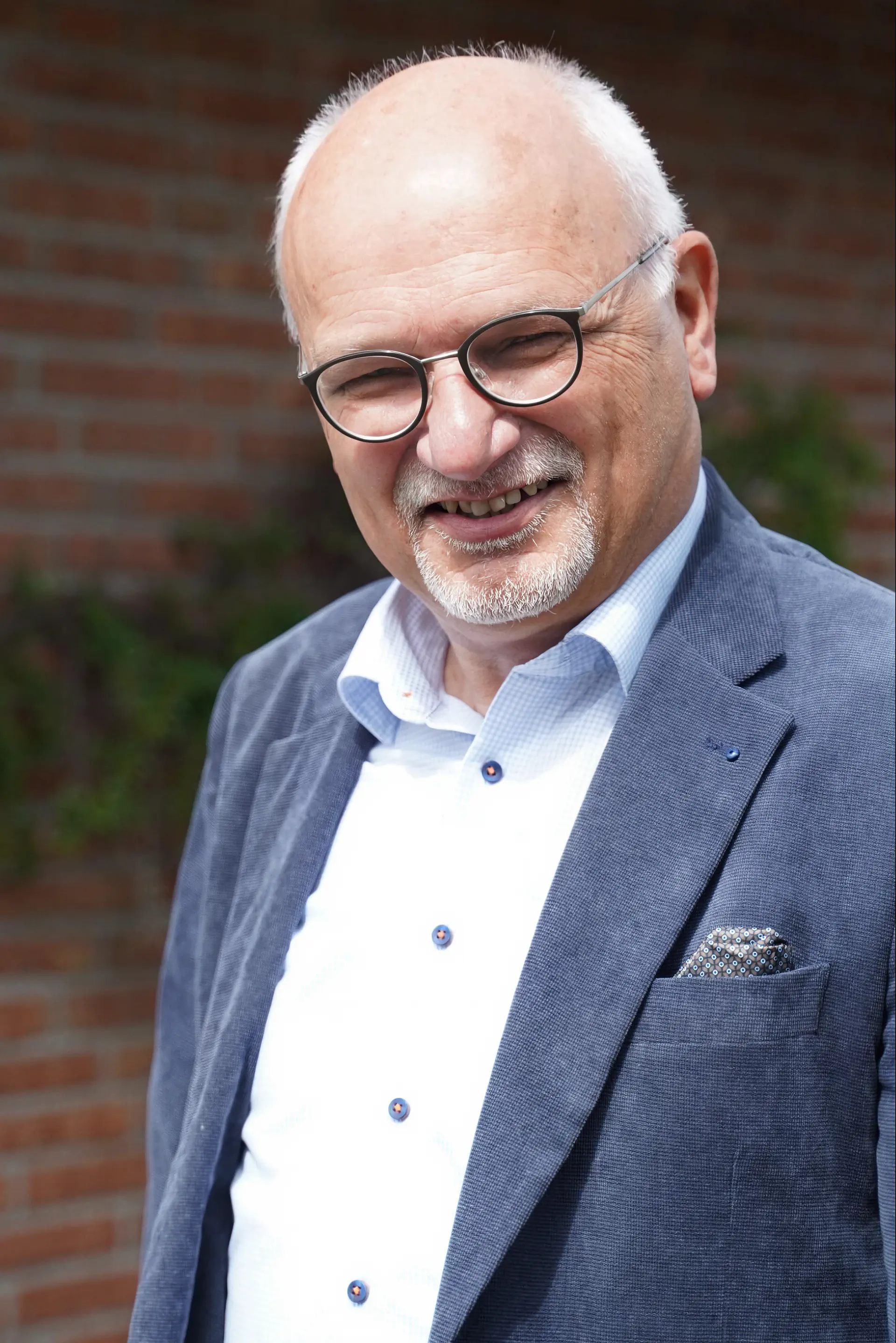 Älterer Mann mit Brille, grauem Haar und Bart, trägt blaues Sakko und weißes Hemd.