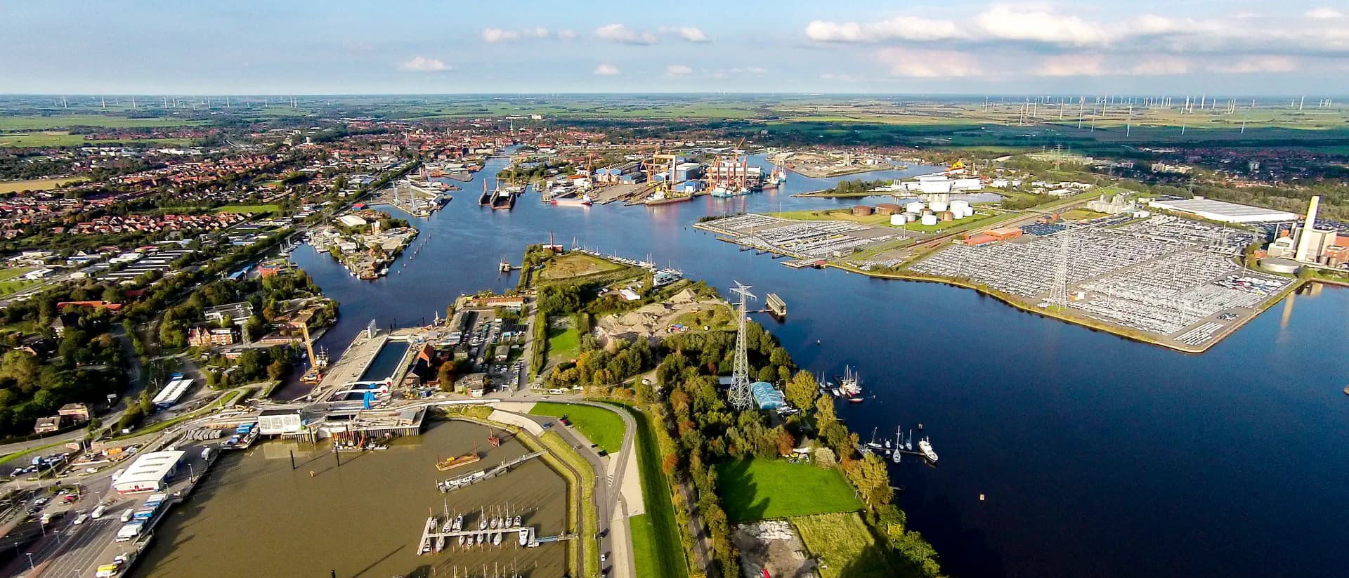 Luftaufnahme eines Hafens mit Schiffen, Autolagern und Windrädern in Emden.