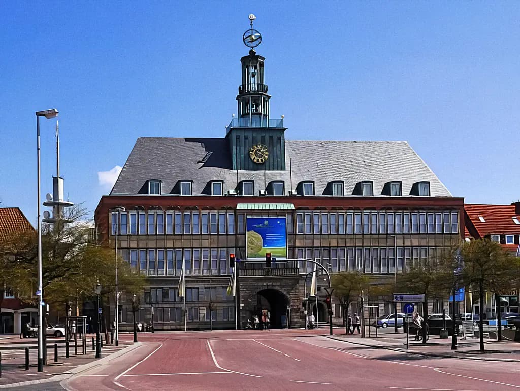 Emder Rathaus mit Turm, Uhr und großem Banner vor blauer Himmelkulisse.