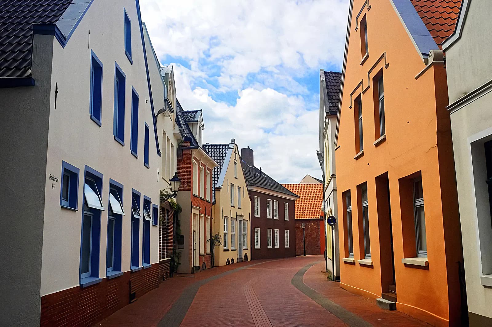 Gasse mit bunten Häusern, Kopfsteinpflaster und blauem Himmel mit Wolken.