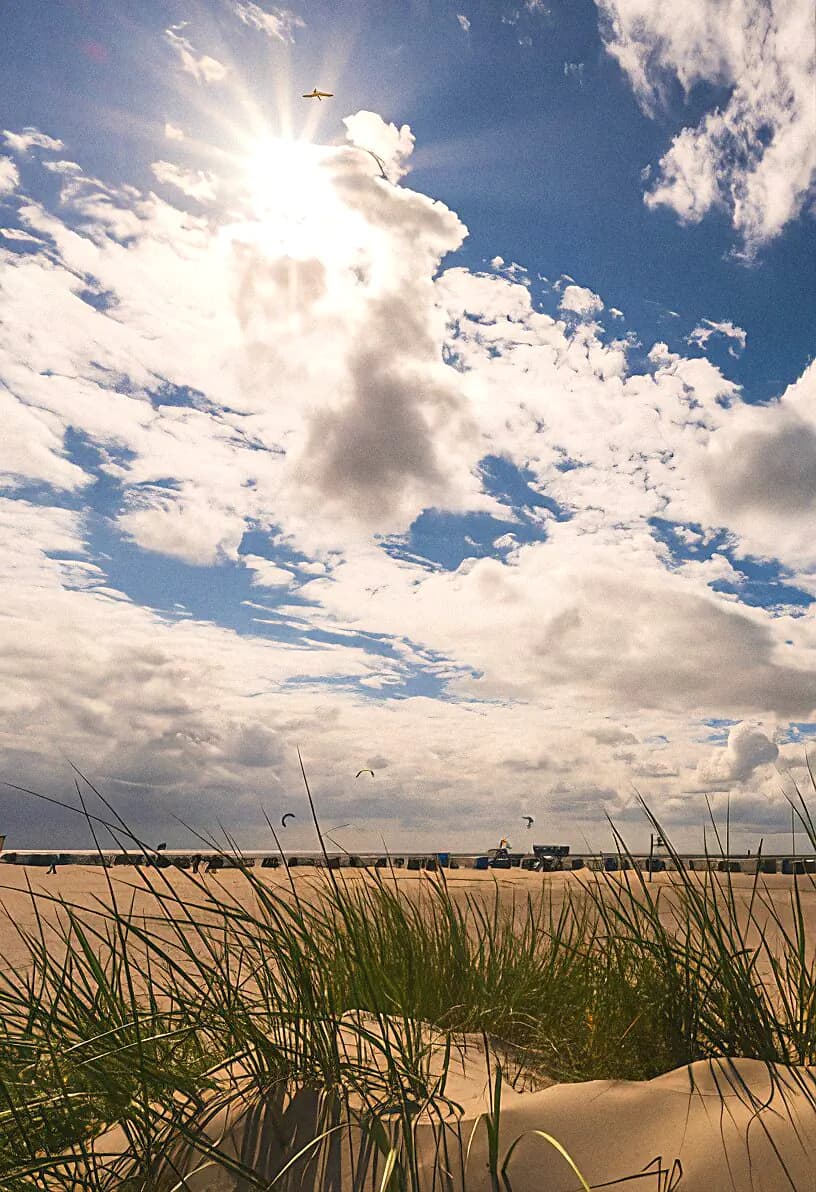 Sonnenschein, Wolken, Strandgras, Kitesurfer und Strandkörbe am Norddeicher Strand.