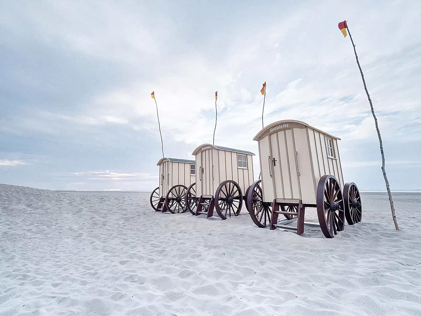 Drei Strandkörbe auf sandigem Strand, Norderney, mit Fahnen im Himmel.